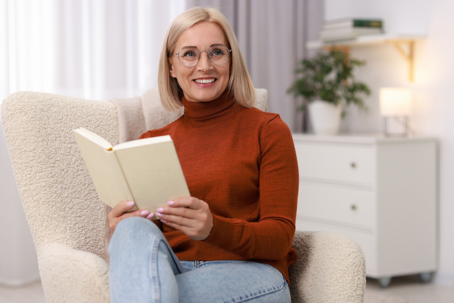 Portrait of smiling middle aged woman reading book on armchair at home